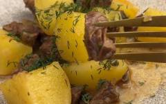 Картошка в казане на плите с мясом говядины, луком и маслом